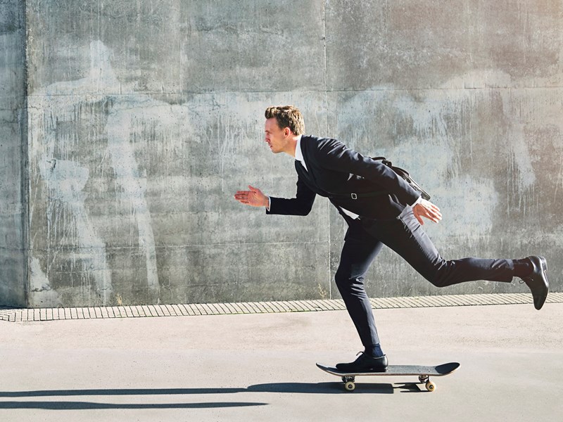 Man i kostym på skateboard.